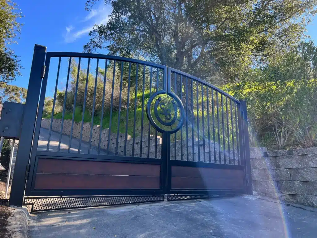 Photo Of A Custom Black Arched Driveway Gate With A Horseshoe Logo On A Sloped Road