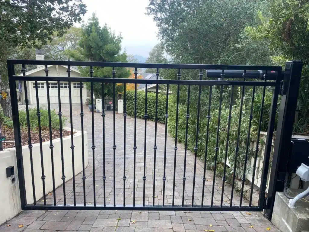 Photo An Automatic Black Wrought Iron Driveway Gate Across A Paved Entry