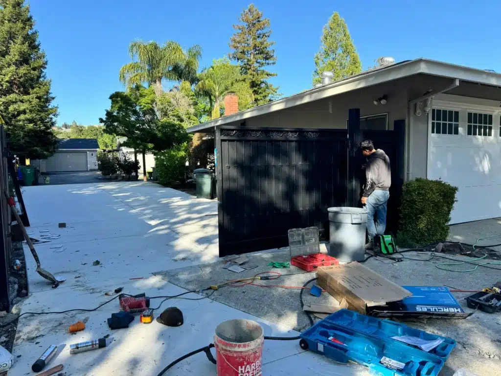 Photo Of A Technician Installing A Large Black Metal Security Driveway Gate On A Property