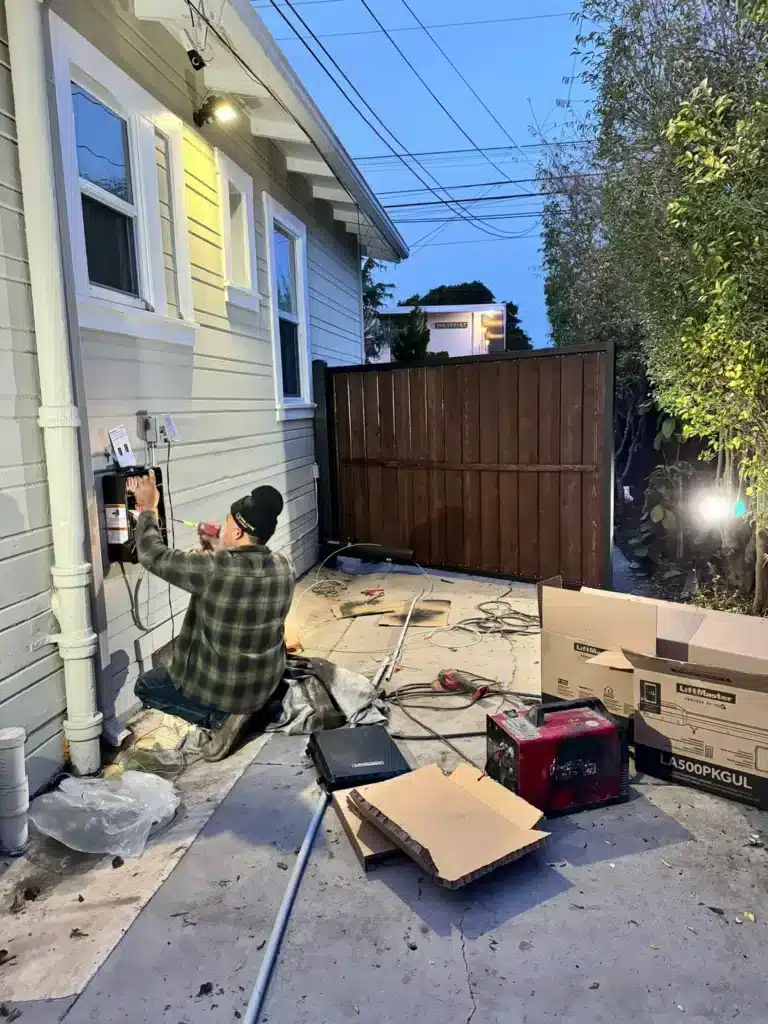 Photo Of Automatic Gate Maintenance Being Done On An Exterior Wall Control Box By A House