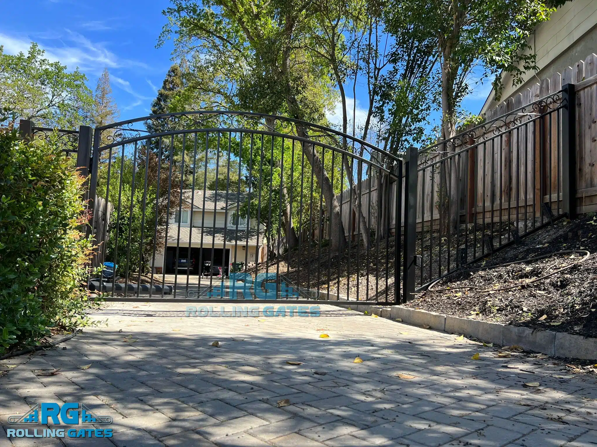 Photo Of Black Wrought Iron Driveway Gate Installed Across A Paved Residential Entry