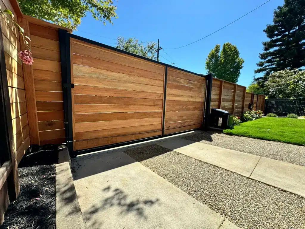 Photo Of Sliding Wooden Privacy Gate With A Modern Black Frame Along A Gravel Driveway